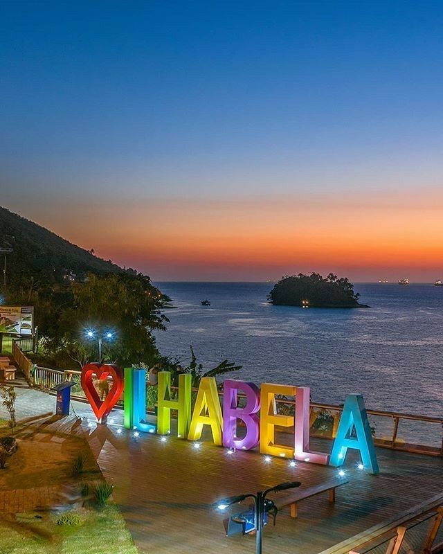 Letreiro colorido Eu Amo Ilhabela ao entardecer com o mar ao fundo